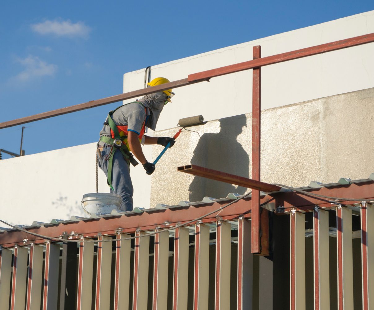 Builder worker painting facade of high-rise building with roller